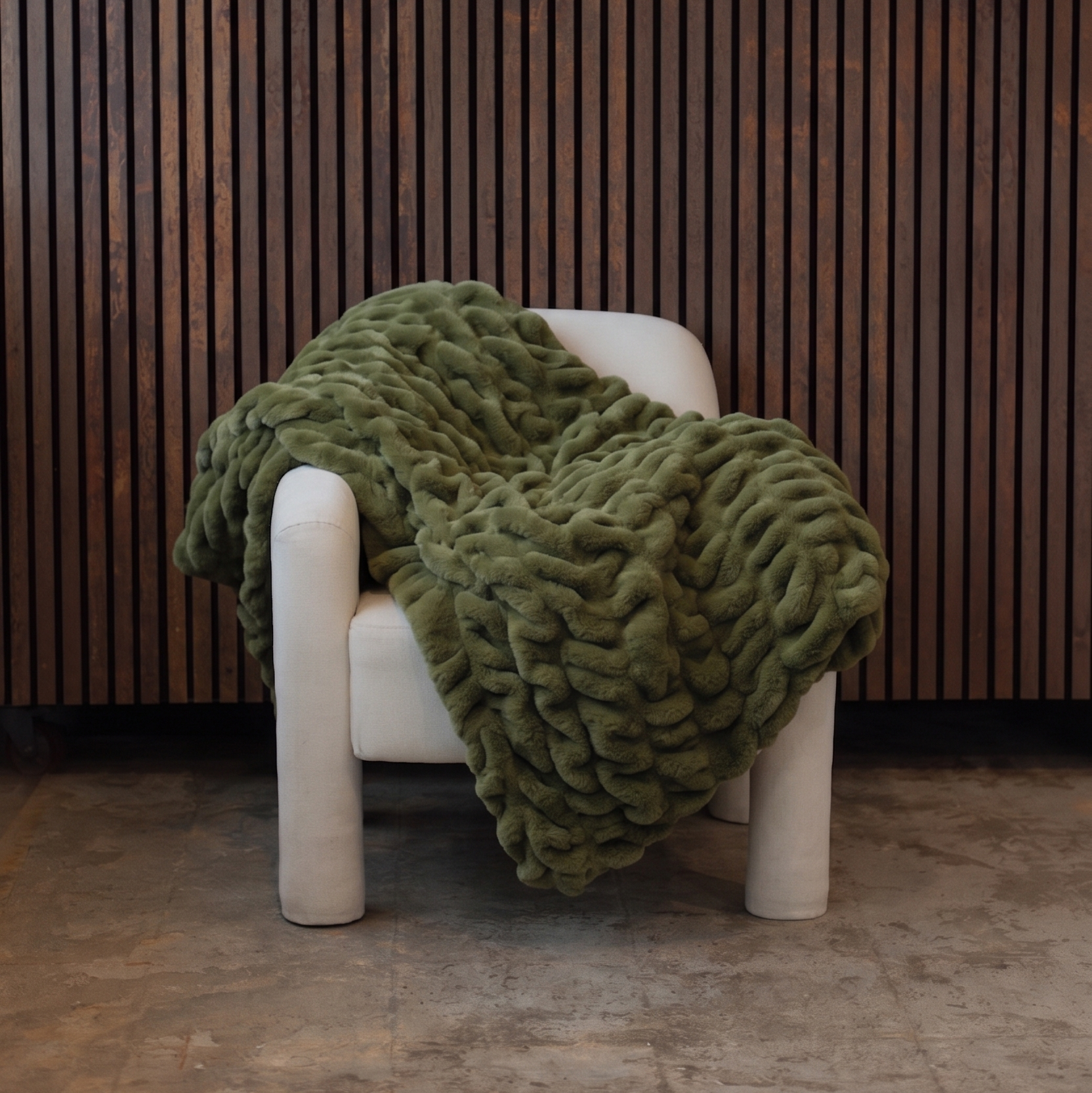 Green textured blanket draped over a white chair against a wooden paneled wall.