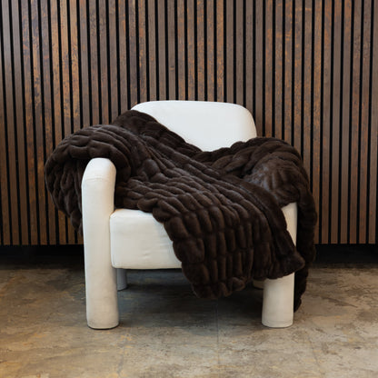 Brown faux fur blanket draped over a white chair against a wooden paneled wall.