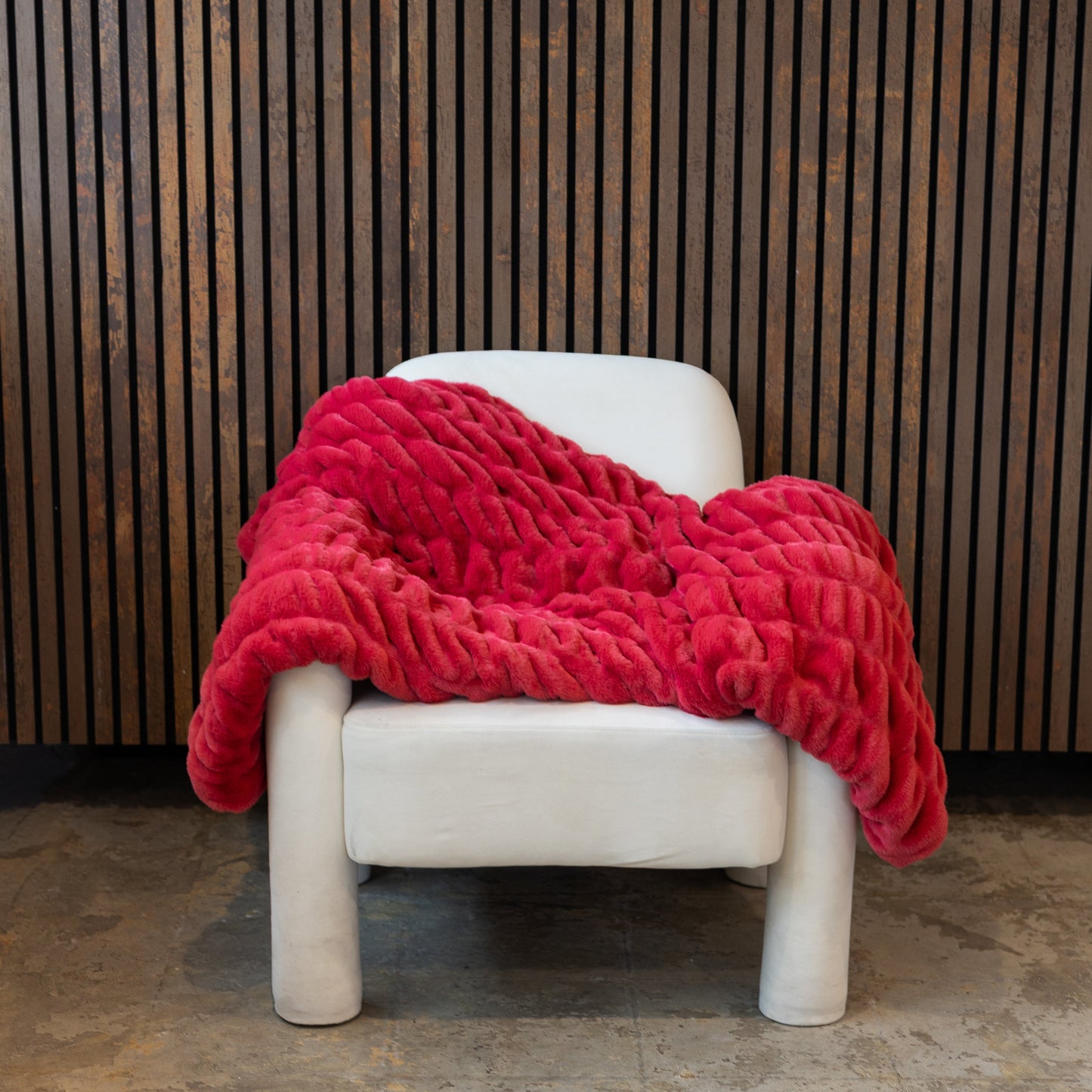 Red blanket draped over a white chair against a wooden paneled wall.