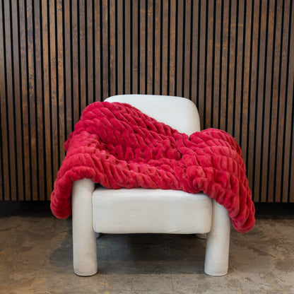 Red blanket draped over a white chair against a wooden paneled wall.